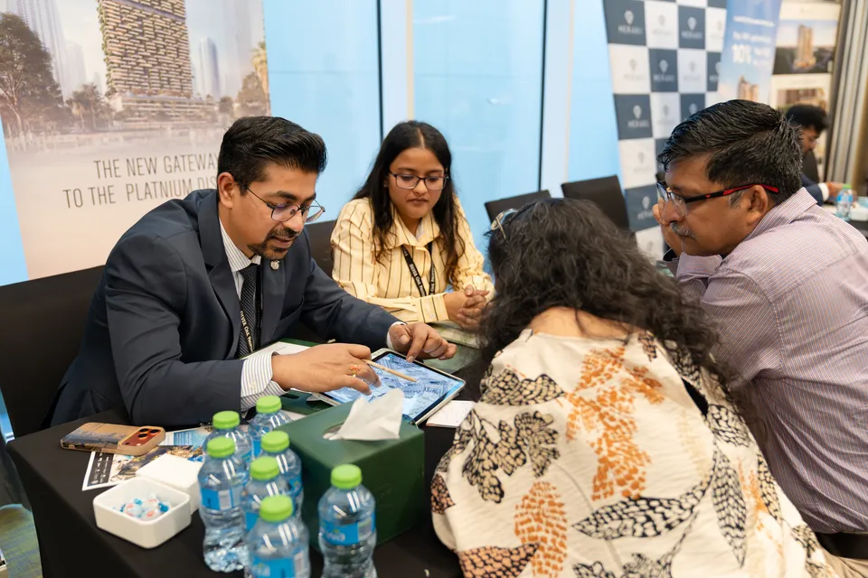 An adviser shows a couple a Dubai project on a tablet at the Dubai Property Expo, in front of a Meraki display