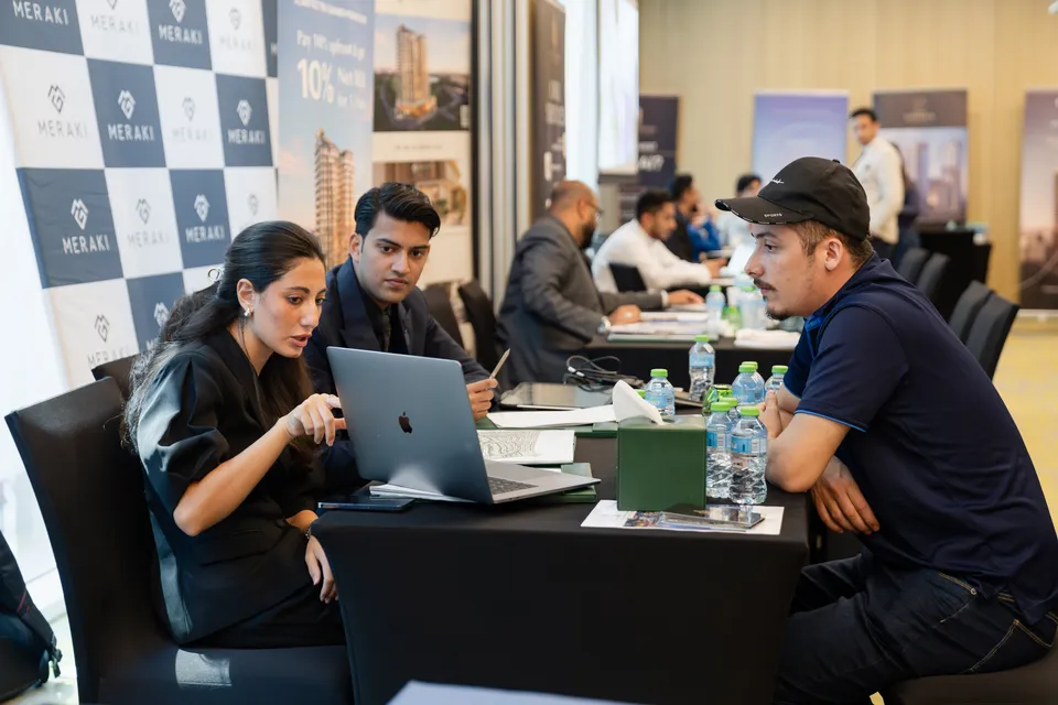 Two advisers show a visitor a project on a laptop at the Meraki stand during the Dubai Property Expo