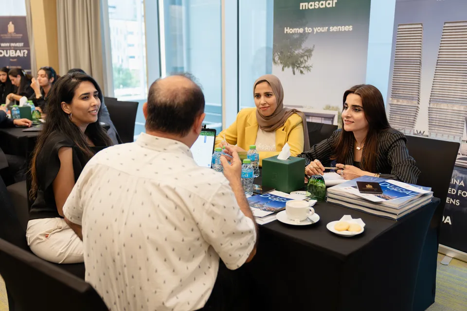 A visitor talks with two advisers over Dubai brochures and coffee, beside a Masaar display