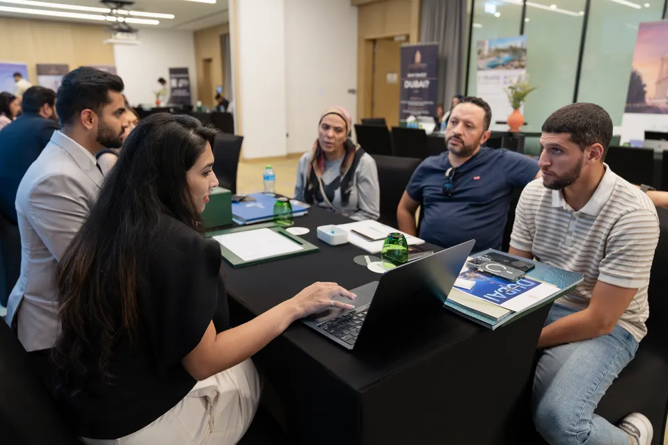 An adviser takes three visitors through a project on a laptop, beneath a "Why invest in Dubai?" banner