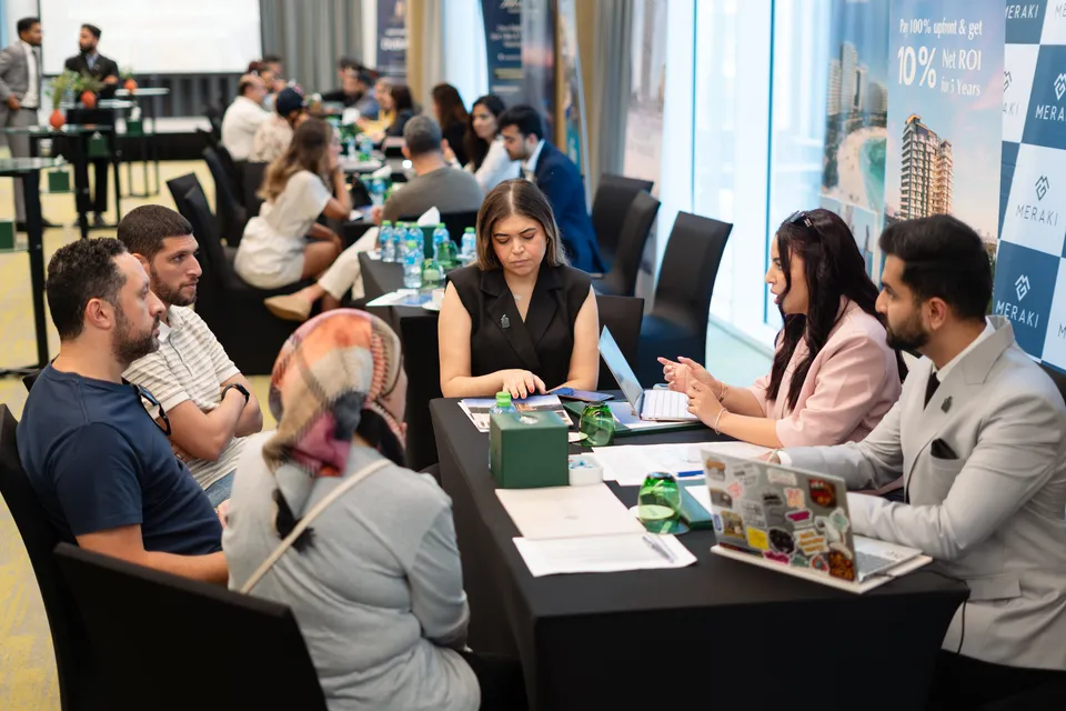 Visitors in consultation at several tables in front of the Meraki display