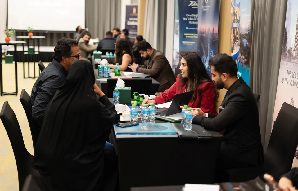 Advisers meet visitors at tables lined with developer banners at the Dubai Property Expo