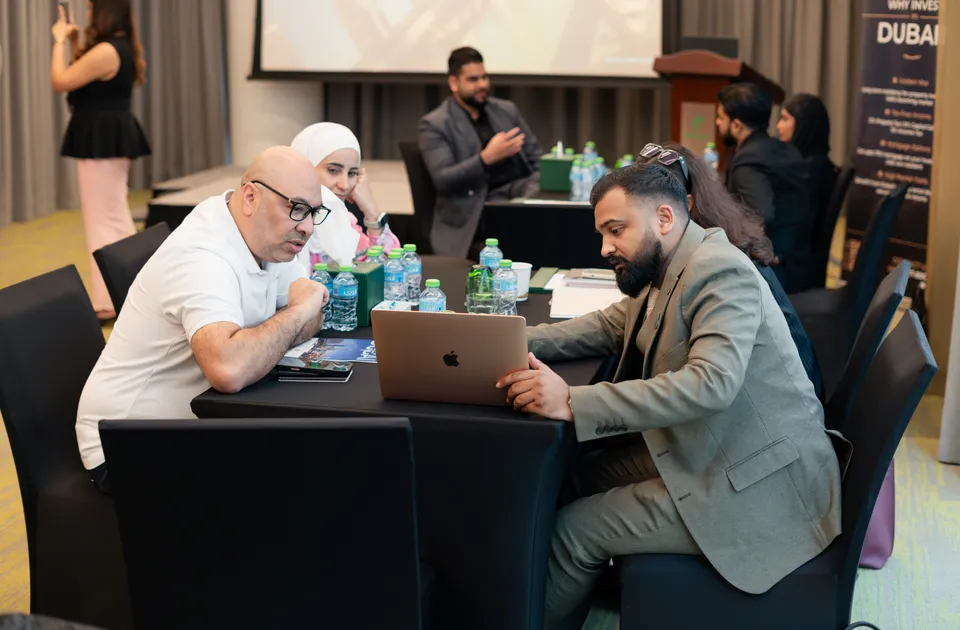 An adviser goes through a project on a laptop with two visitors, near the presentation stage