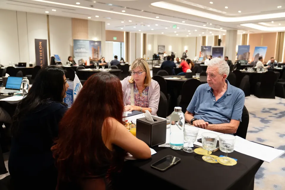 In the foreground, two advisers consult with an older couple, with the busy expo floor and a Pantheon banner behind them