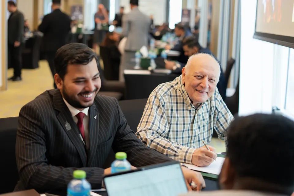 Laughing together at a consultation table, an adviser and a visitor share a moment while laptops sit open between them
