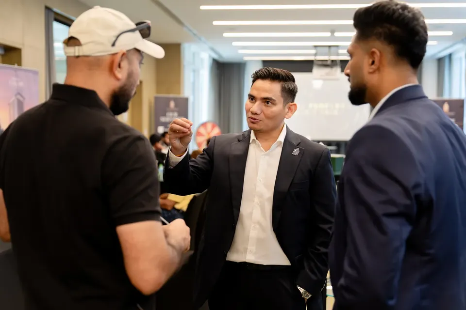 Three men in business attire talk standing up in a hallway lined with branded pull-up banners at the expo