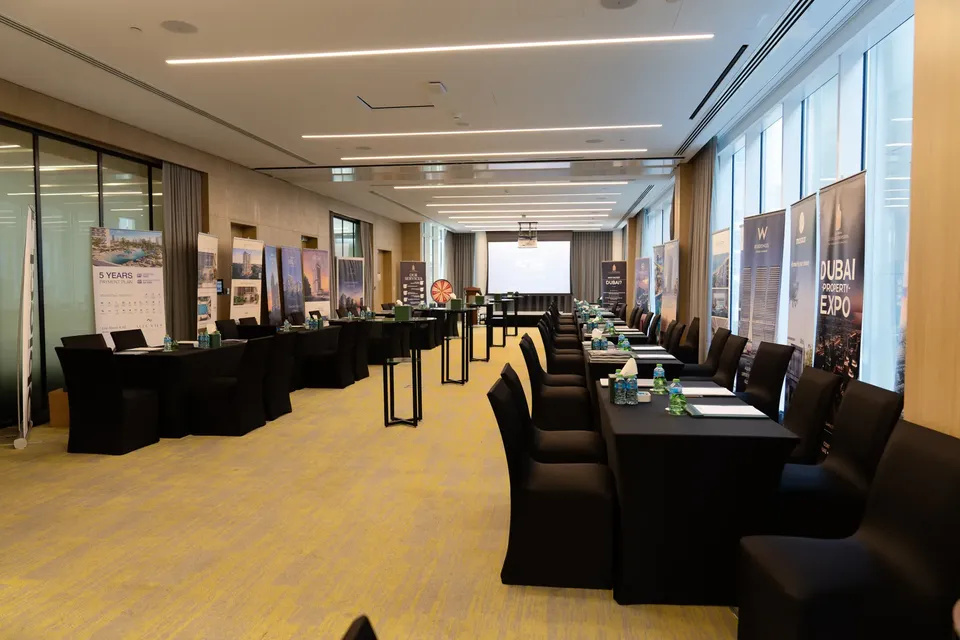 Rows of empty chairs and desks face a screen in a conference room set up for the expo, banners lining the windows