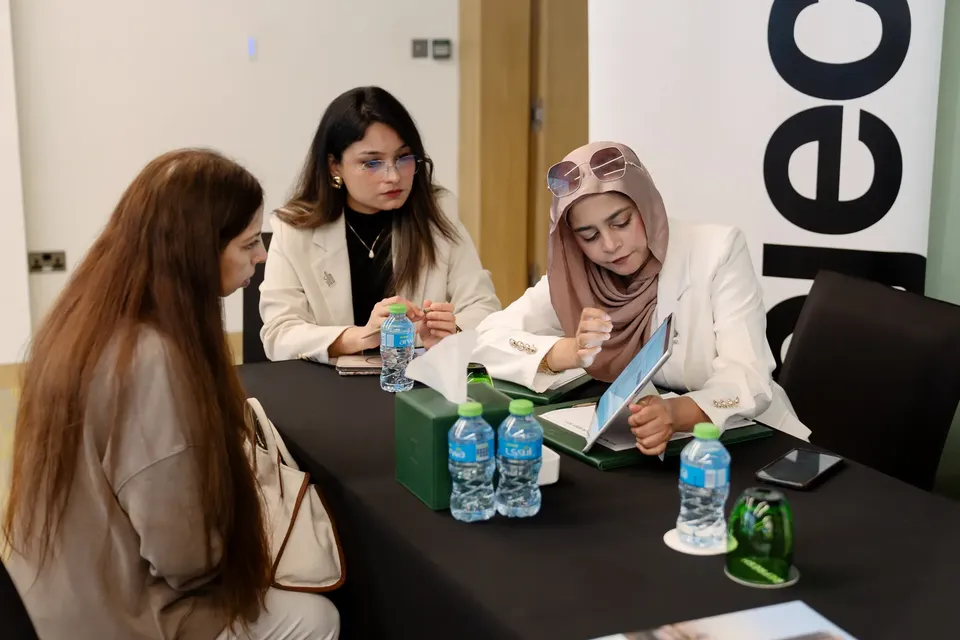 Three women review documents and a tablet together at a consultation table, water bottles and a tissue box in front of them