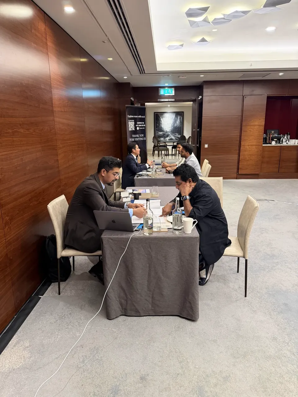 Advisers meet with visitors at tables along a wood-panelled corridor, near a thank-you and contact banner