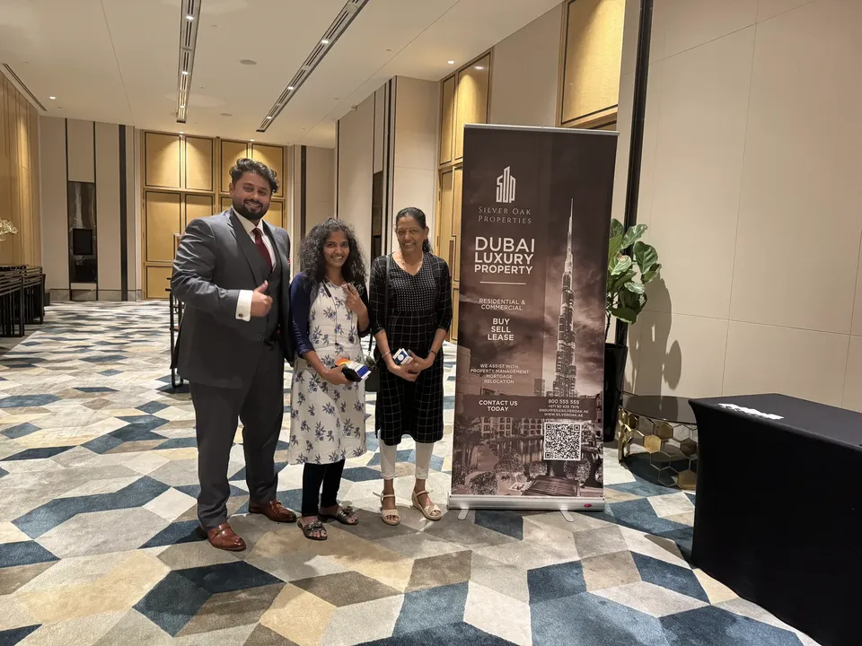 Three people pose together in a hallway beside a Silver Oak Properties banner at the expo