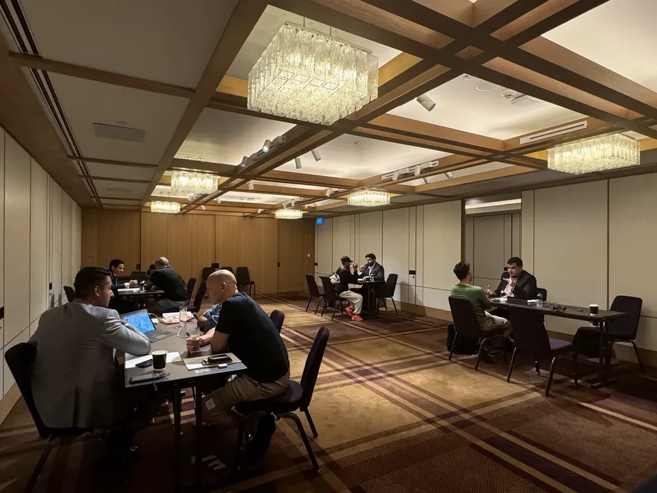 Multiple consultation tables are arranged under a coffered, chandelier-lit ceiling at the property expo