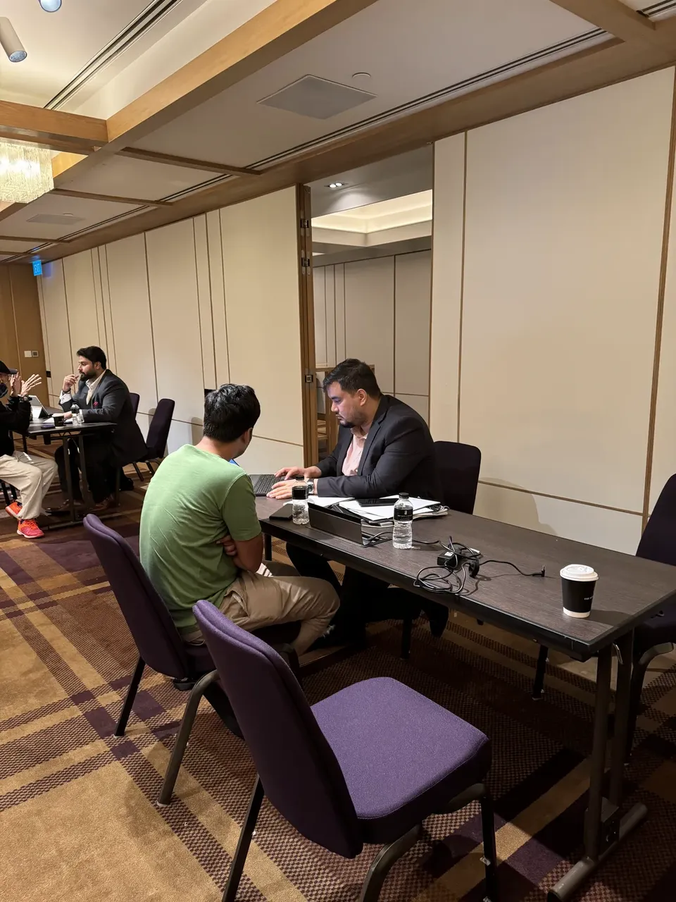 A visitor in a green shirt talks with an adviser typing on a laptop at a side table at the expo