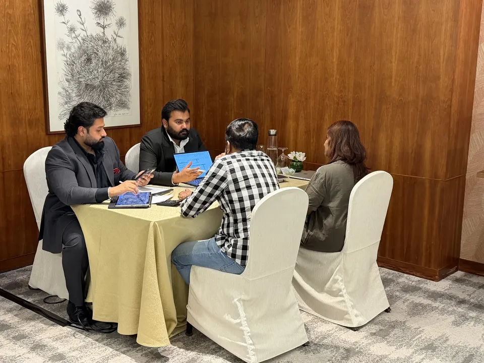 Two advisers meet with a seated couple at a round table, tablets and a folder laid out between them
