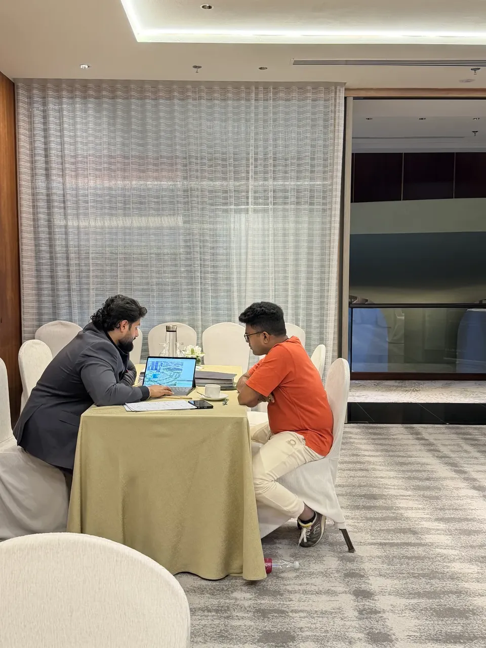 A visitor in an orange t-shirt looks on as an adviser points to a property map on a laptop screen
